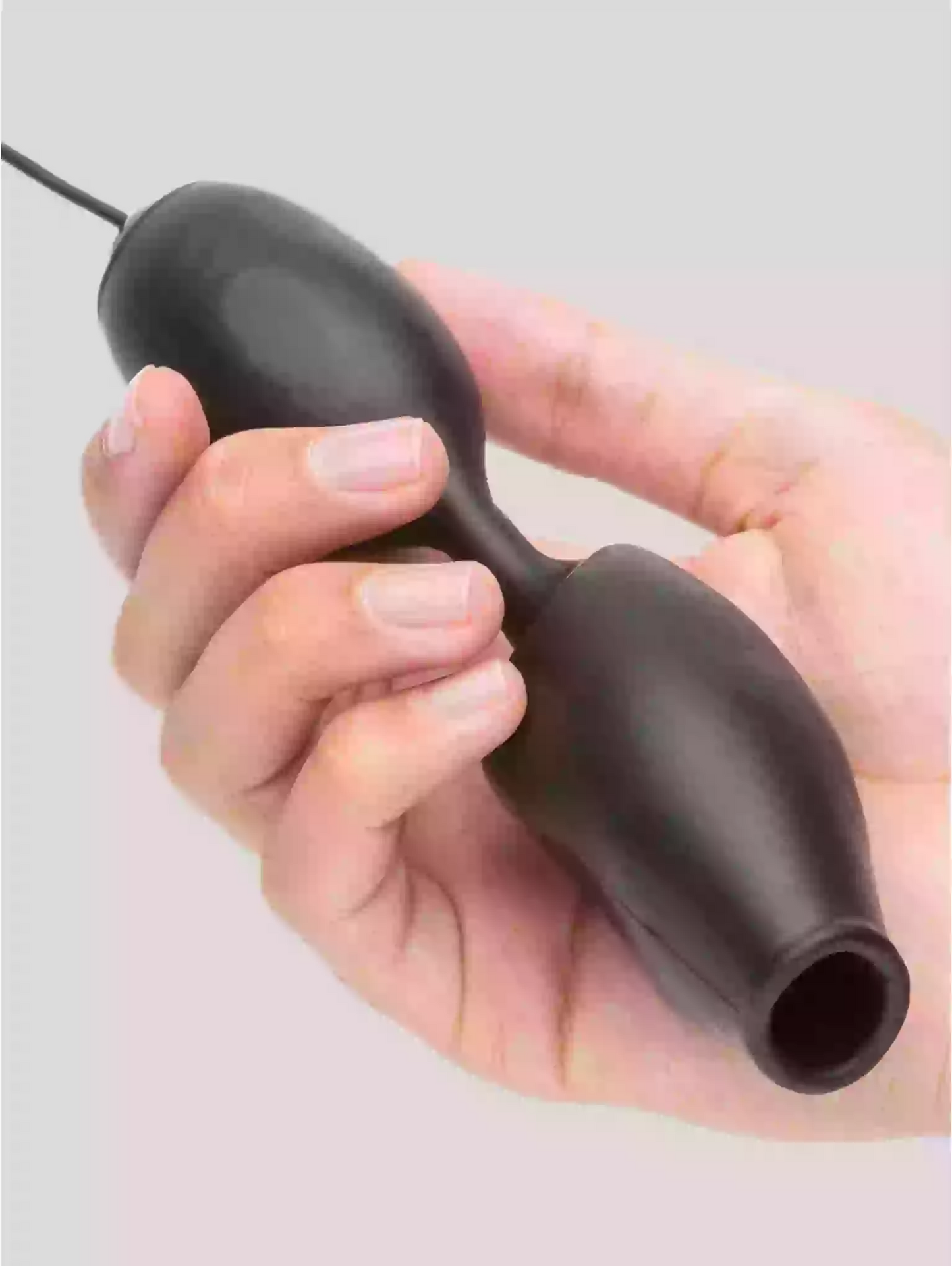 Hand holding a black silicone butt plug against a light gray background
