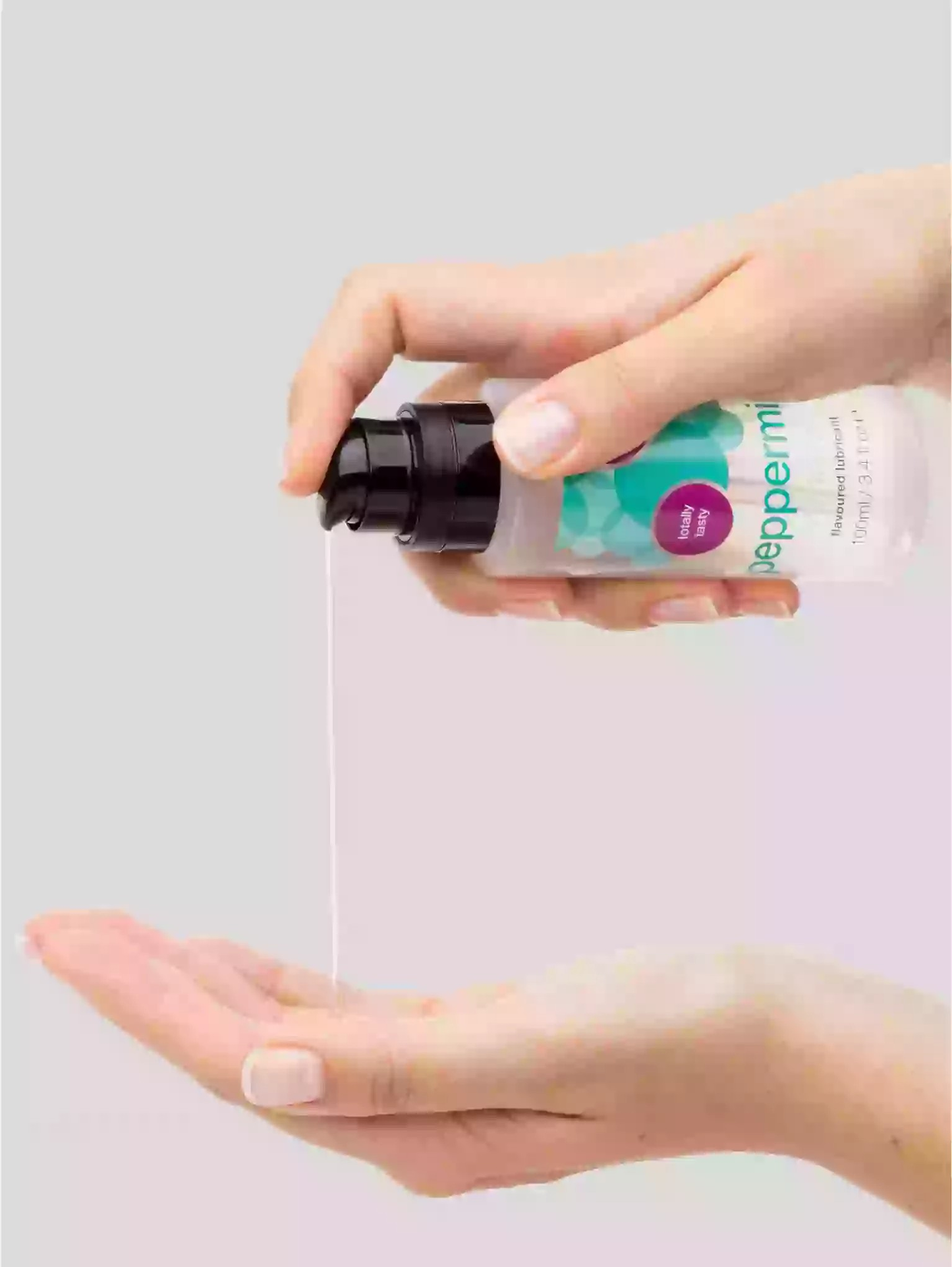 Hand holding a small spray bottle with a clear liquid over an open palm on a light gray background