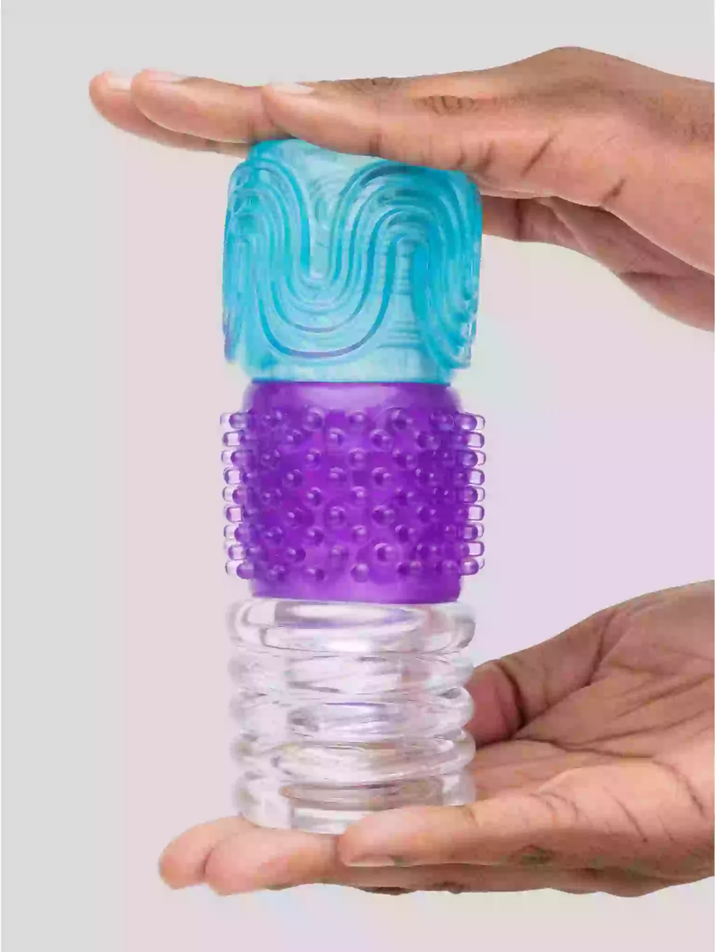 Hand holding a cylindrical massager with blue top and purple middle section on a light gray background