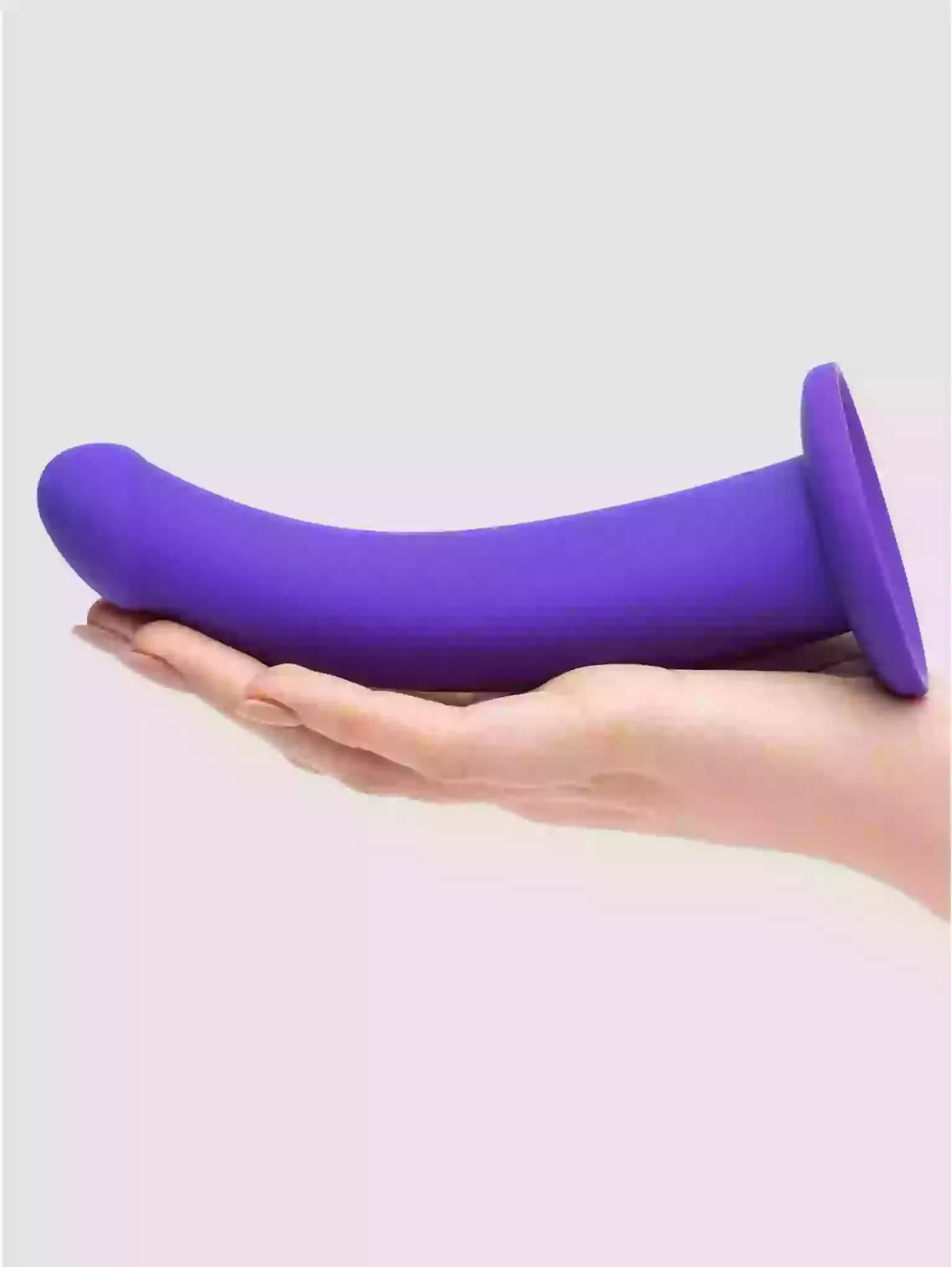 Purple silicone product held in a hand against a light gray background