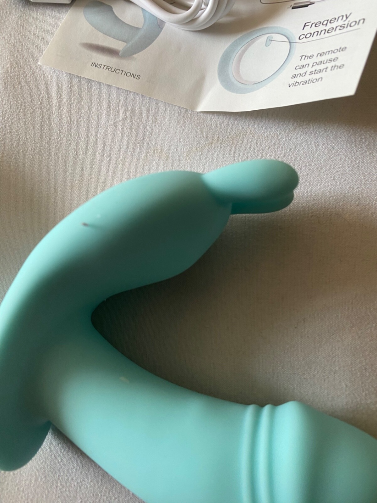 Turquoise silicone remote control on a beige surface with packaging in the background