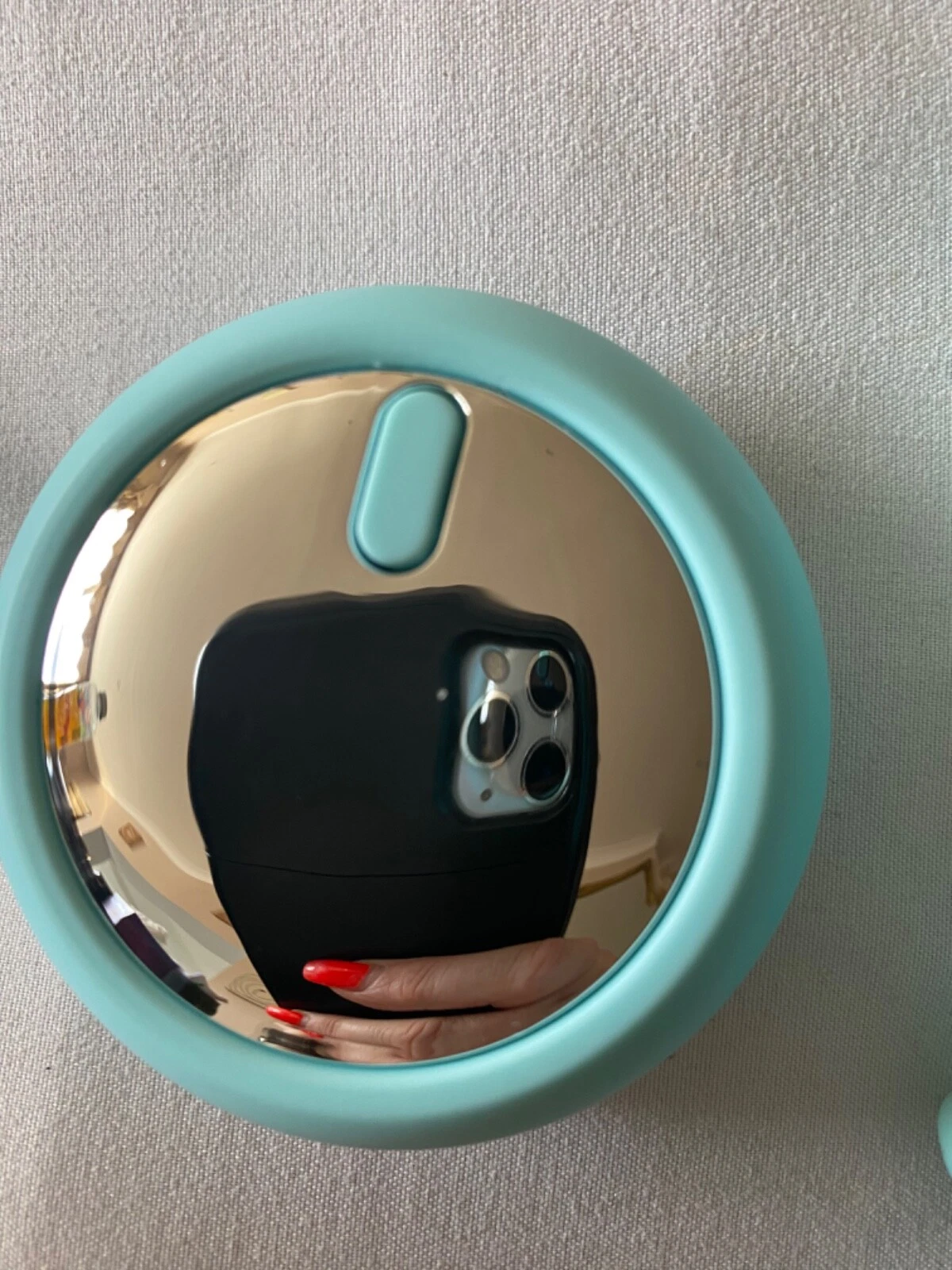 Teal round mirror reflecting a phone with a black case on a light gray background
