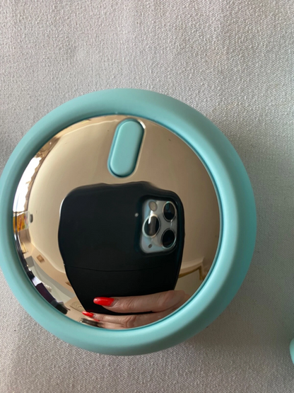 Teal round mirror reflecting a phone with a black case on a light gray background
