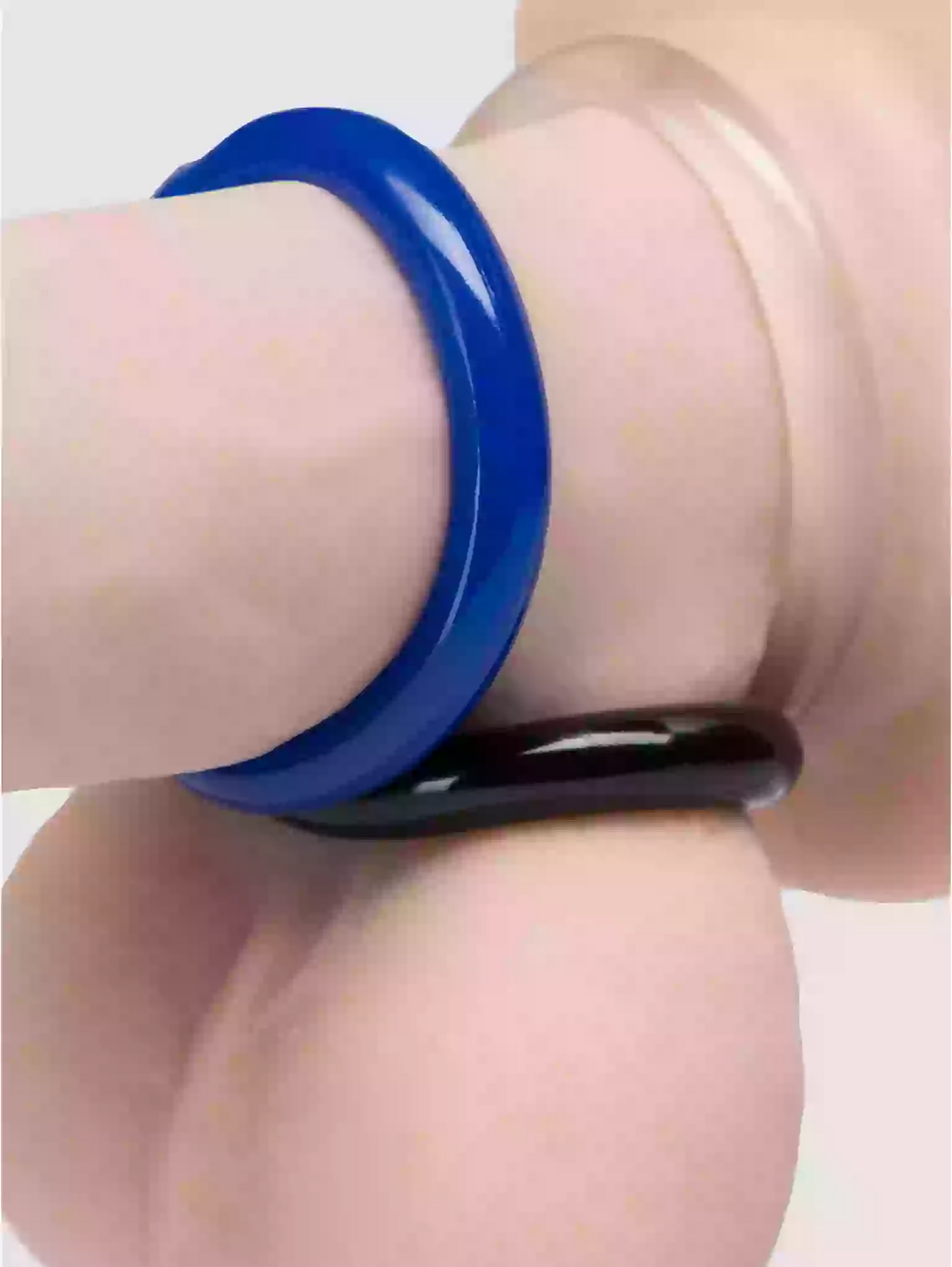 Blue and black rings on a person's finger against a light background