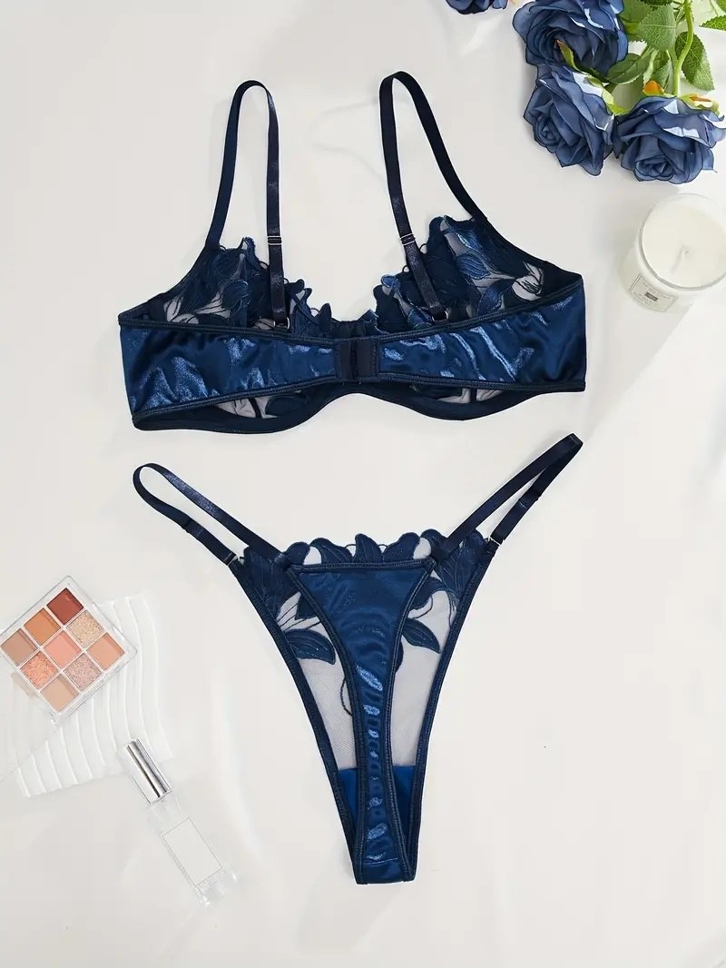 Blue lace lingerie set on a white surface with flowers and makeup products.