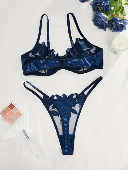 Blue lace lingerie set on a white surface with flowers and makeup products.