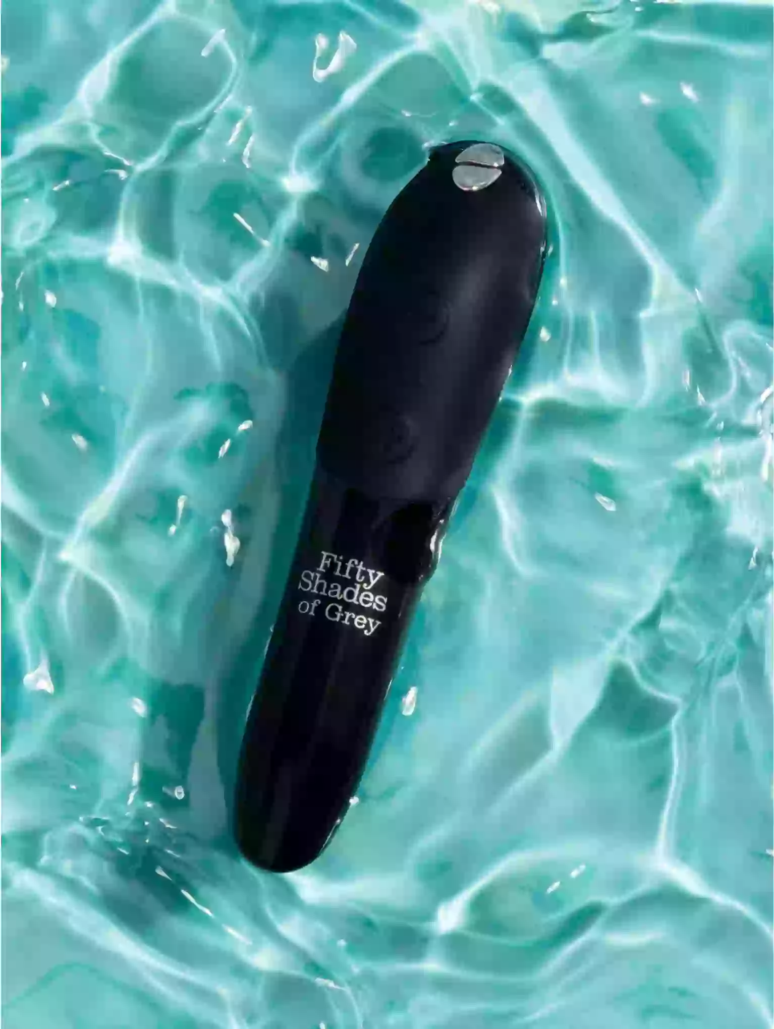 Black object with 'Fifty Shades of Grey' text floating in clear blue water.
