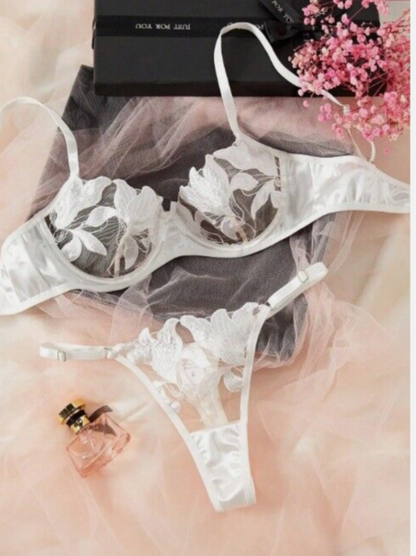 White lace lingerie set on a soft pink background with a perfume bottle and flowers.
