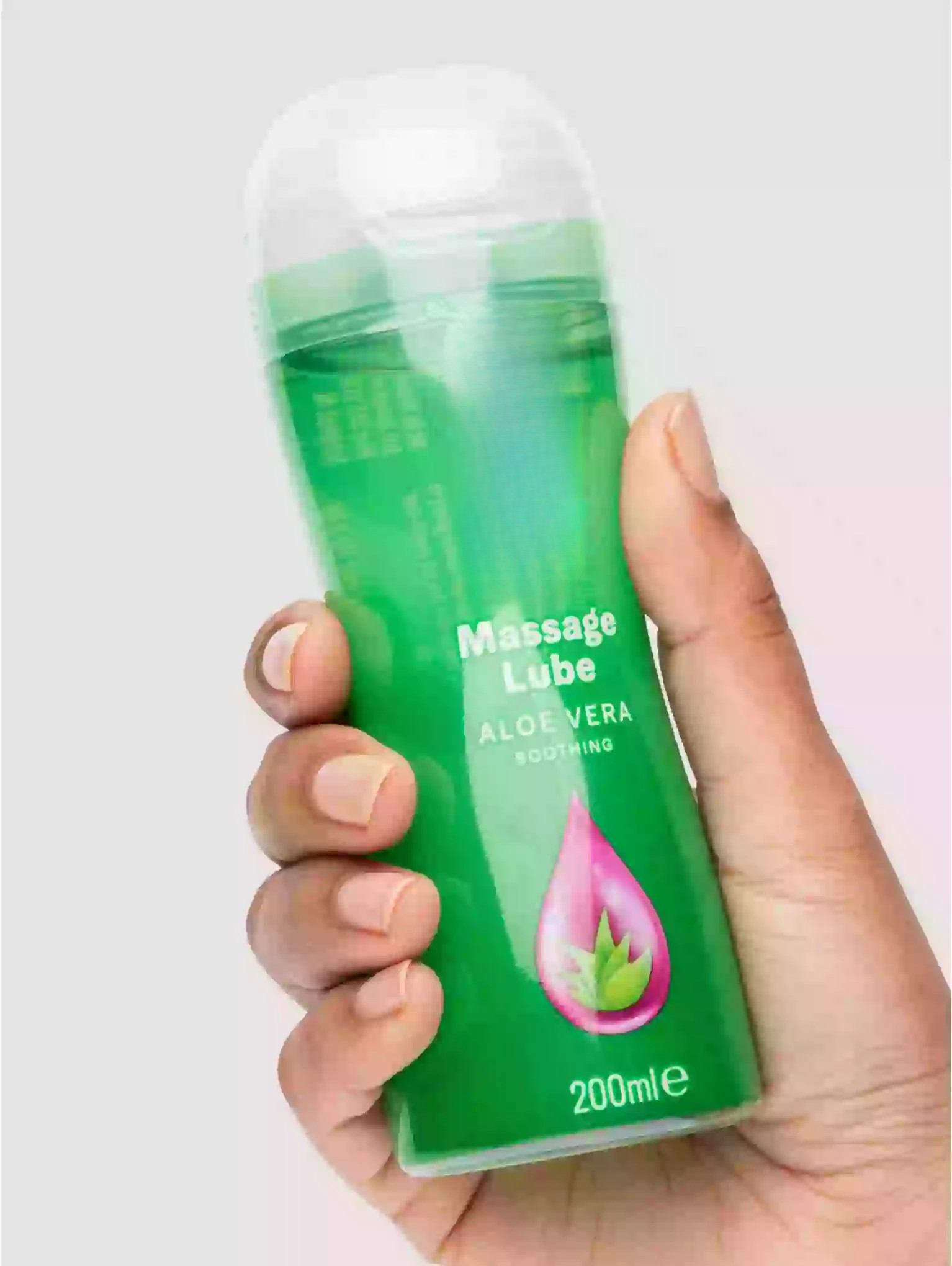 Hand holding a bottle of massage lube labeled 'Aloe Vera' on a light background