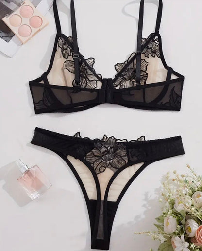 Black lace lingerie set on a white background with a small bouquet of flowers and perfume bottle.