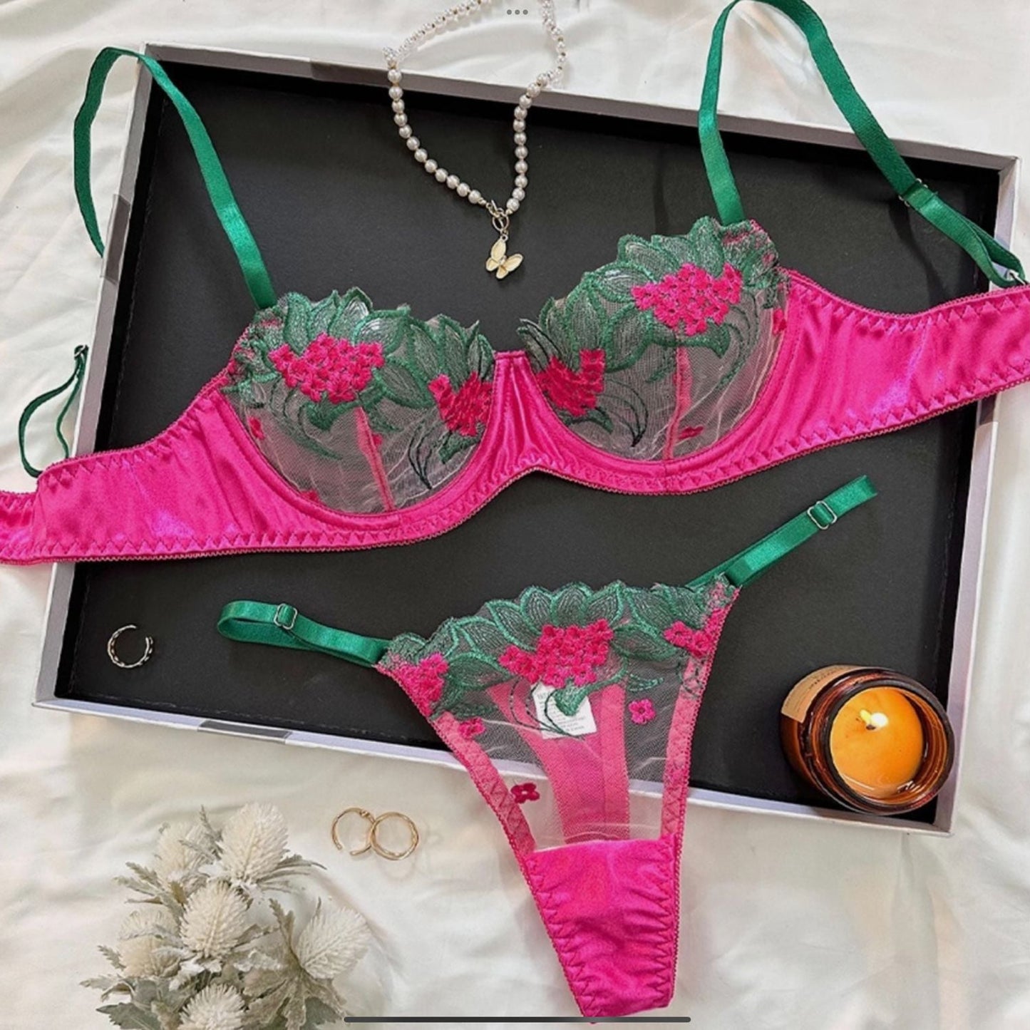 Pink and green lingerie set with jewelry on a black tray.