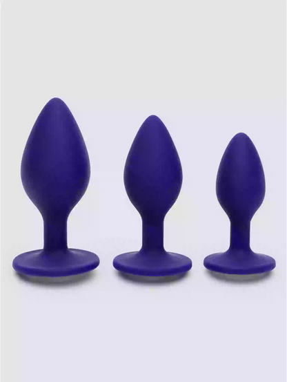 Three purple silicone butt plugs of different sizes on a white background