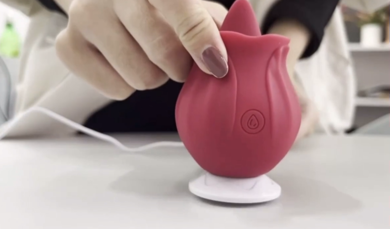 Person holding a pink silicone product with a white base on a light surface.