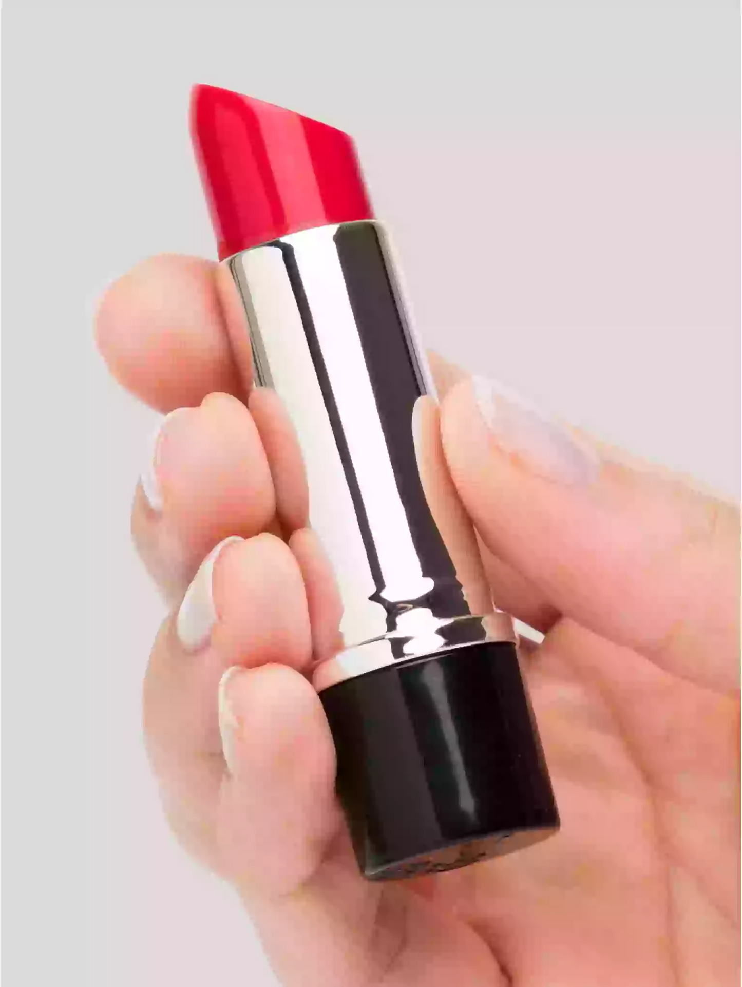 Red lipstick held in a hand against a light gray background