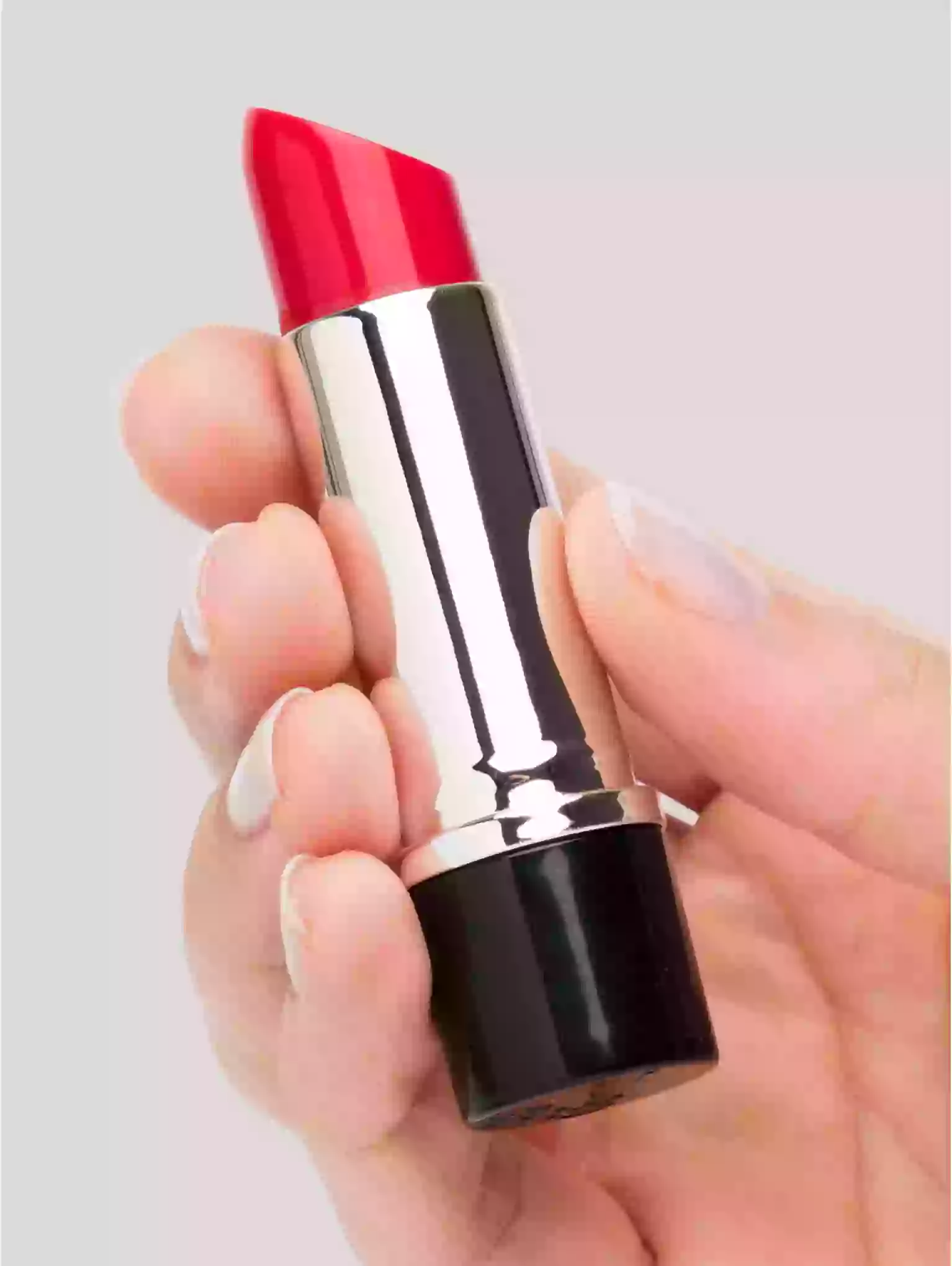 Red lipstick held in a hand against a light gray background