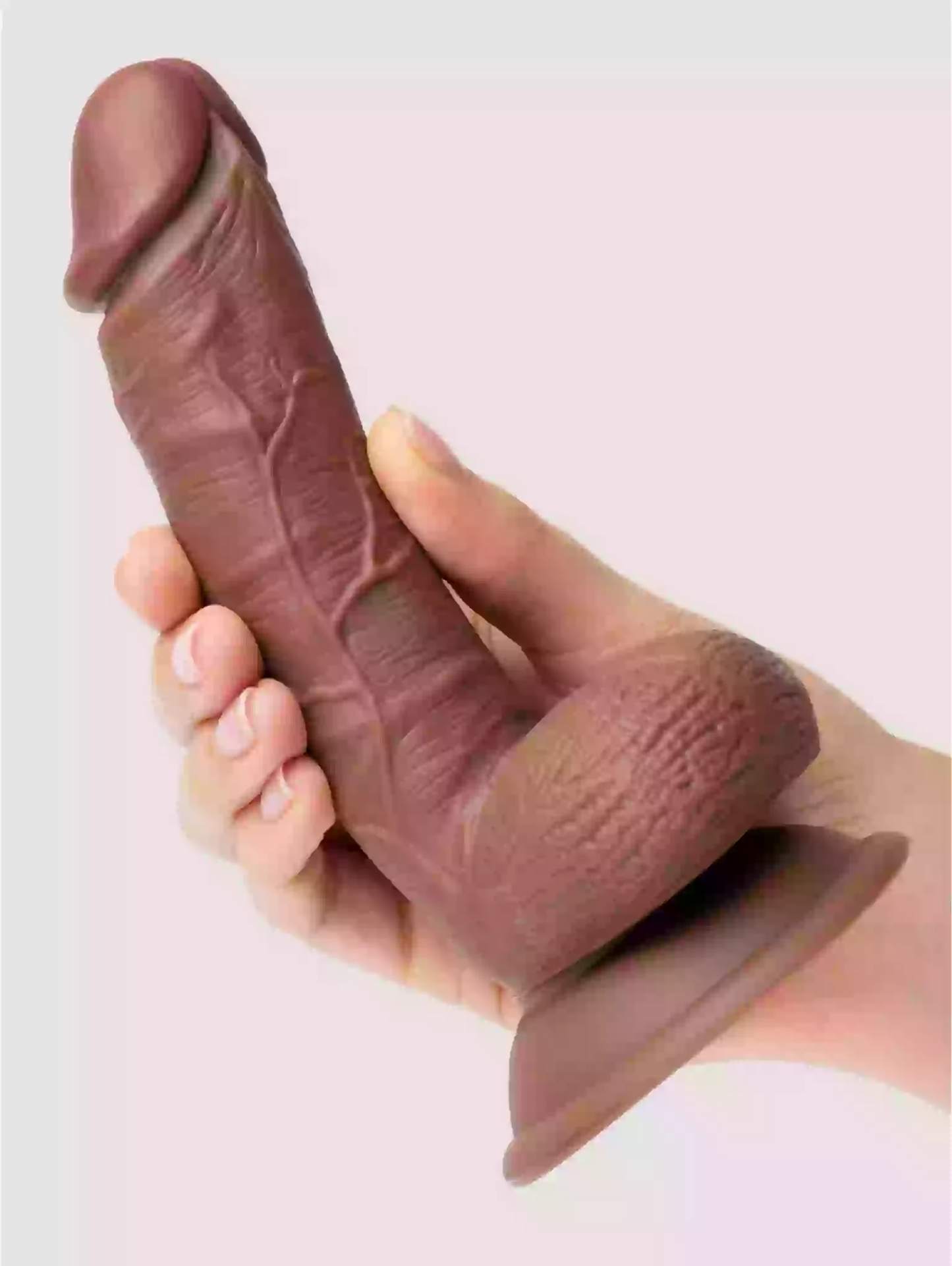 Hand holding a realistic silicone model of a penis against a light pink background