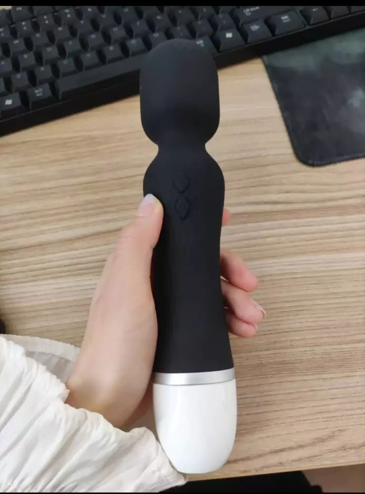 Hand holding a black and silver handheld device on a desk with a keyboard in the background