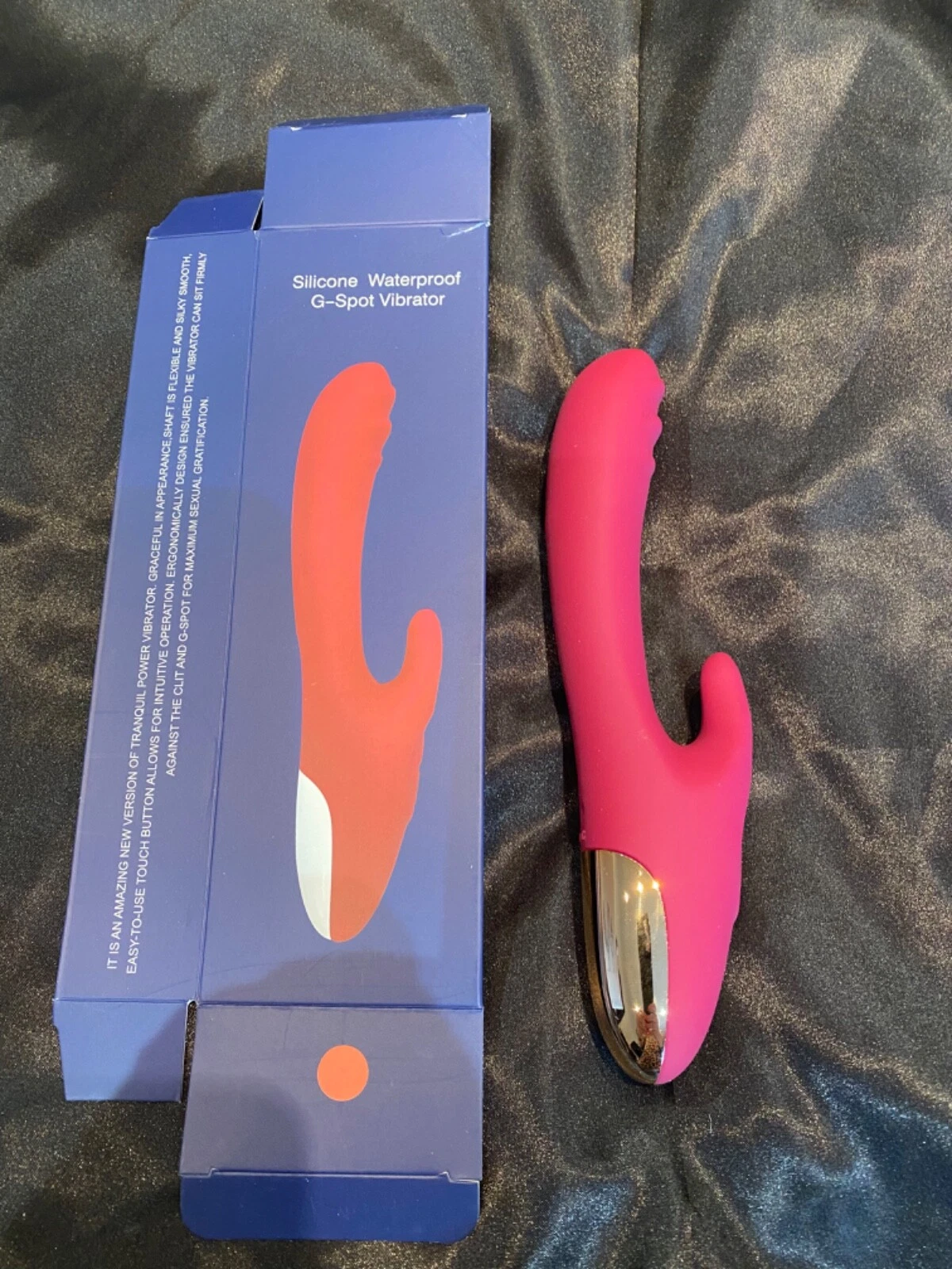 Pink silicone G-Spot vibrator next to its packaging on a textured surface