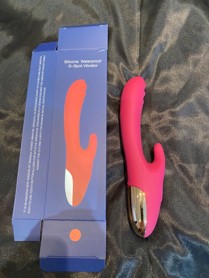 Pink silicone G-Spot vibrator next to its packaging on a textured surface
