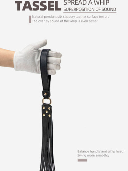 Black leather whip with tassels held by a gloved hand on a white background