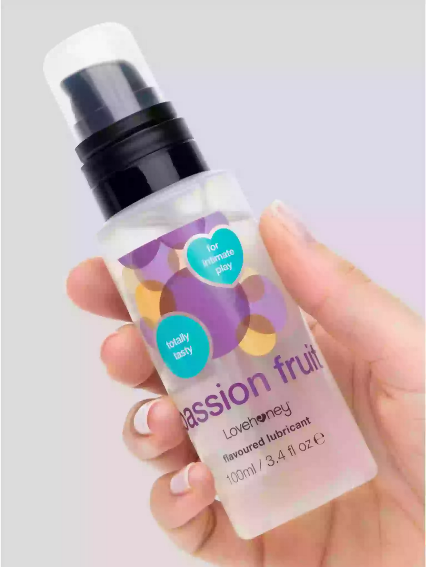 Hand holding a bottle of Lovehoney passion fruit flavored lubricant against a light background