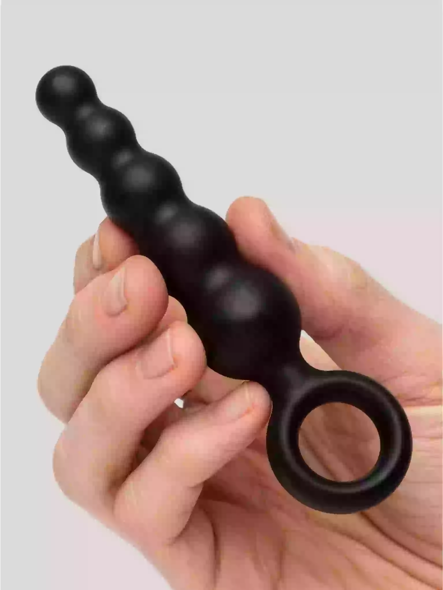 Black silicone butt plug held in a hand against a light gray background