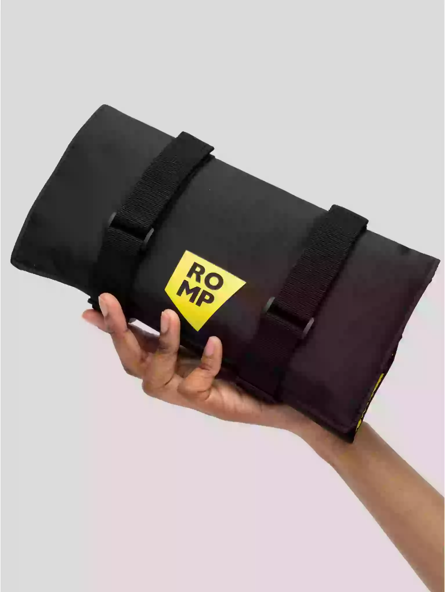 Black roll-up bag with a yellow logo held by a hand on a light gray background