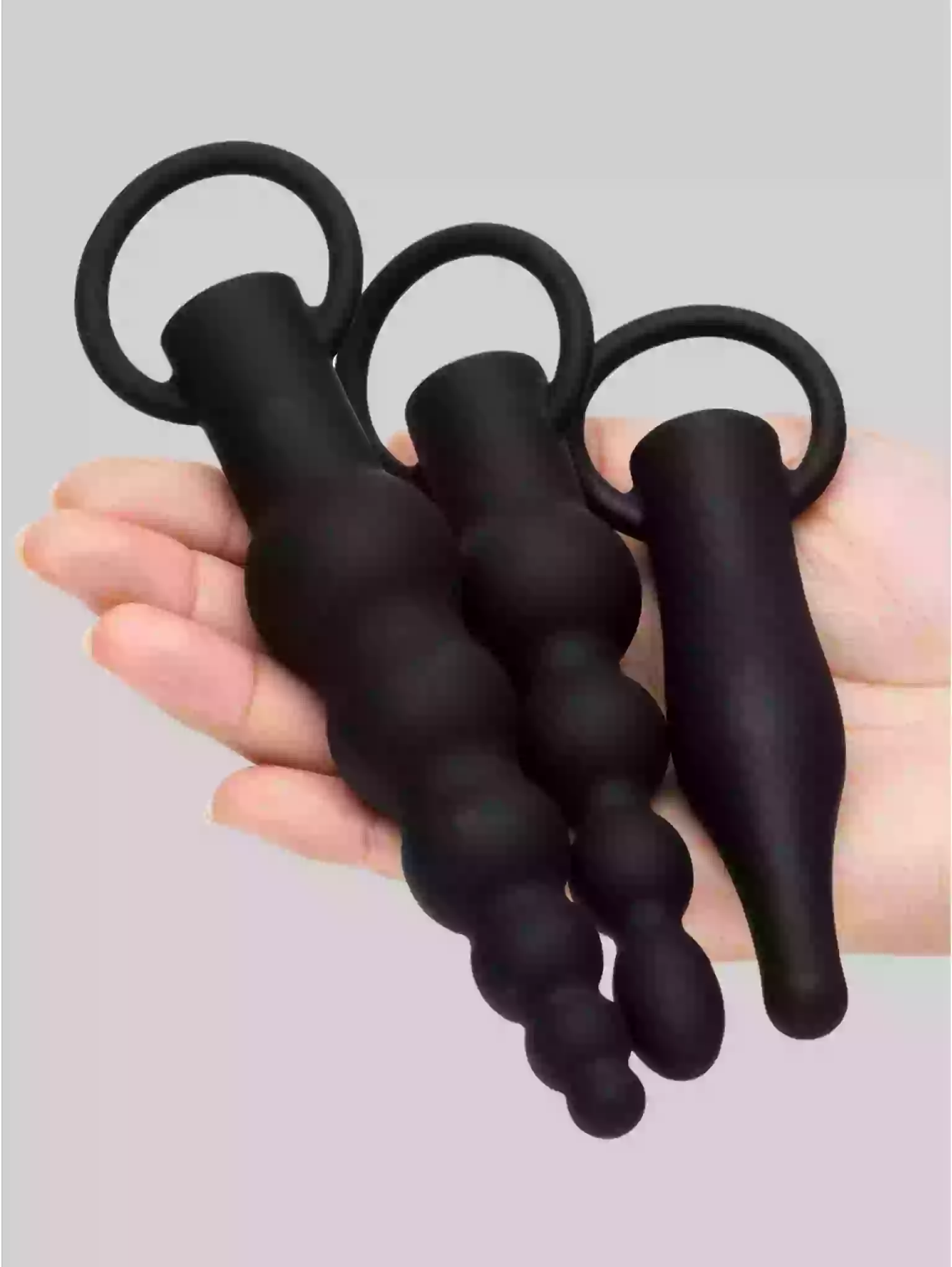 Black silicone butt plug set held in a hand against a gray background