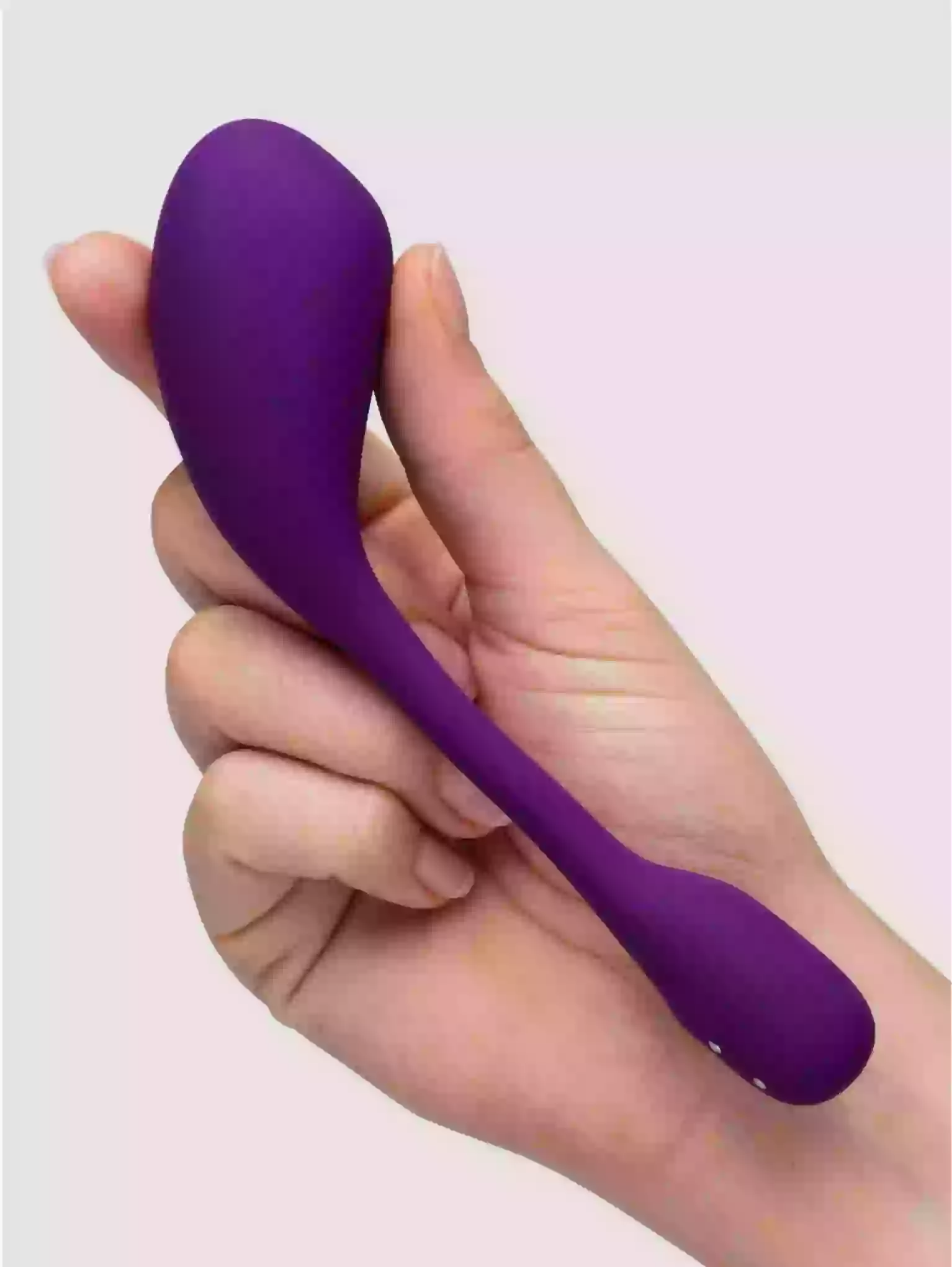 Purple handheld massager held in a hand against a light purple background