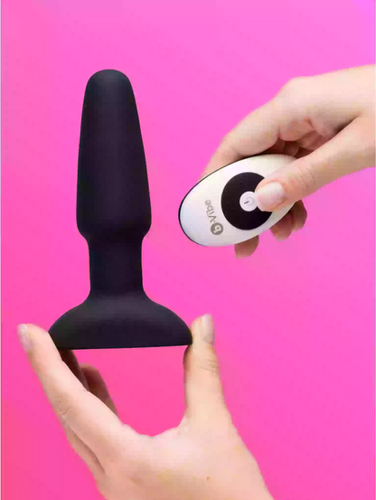Black silicone product held by a hand with a remote control on a pink background