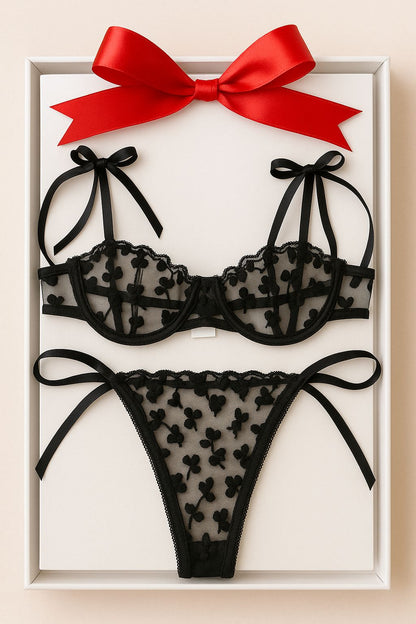 Black lace lingerie set with a red bow in a white box on a beige background