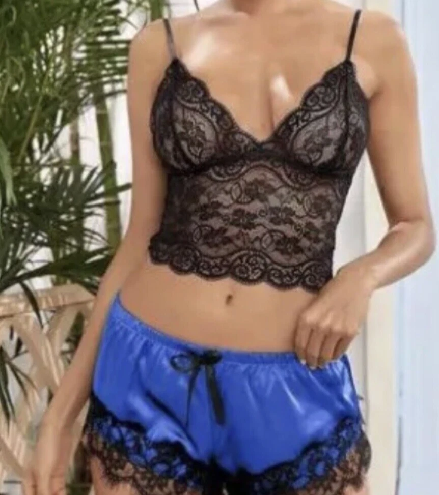 Person wearing a black lace bra and blue satin shorts with a plant in the background