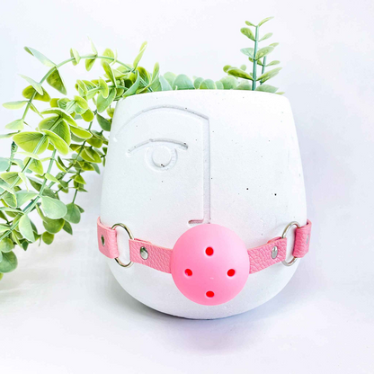 White planter with pink face mask and green plant on a white background