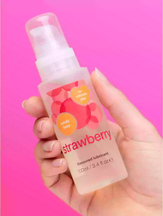 Hand holding a strawberry-flavored lubricant bottle against a pink background