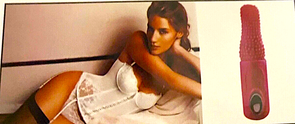 Woman lying on a bed with a pink and red massager next to her.