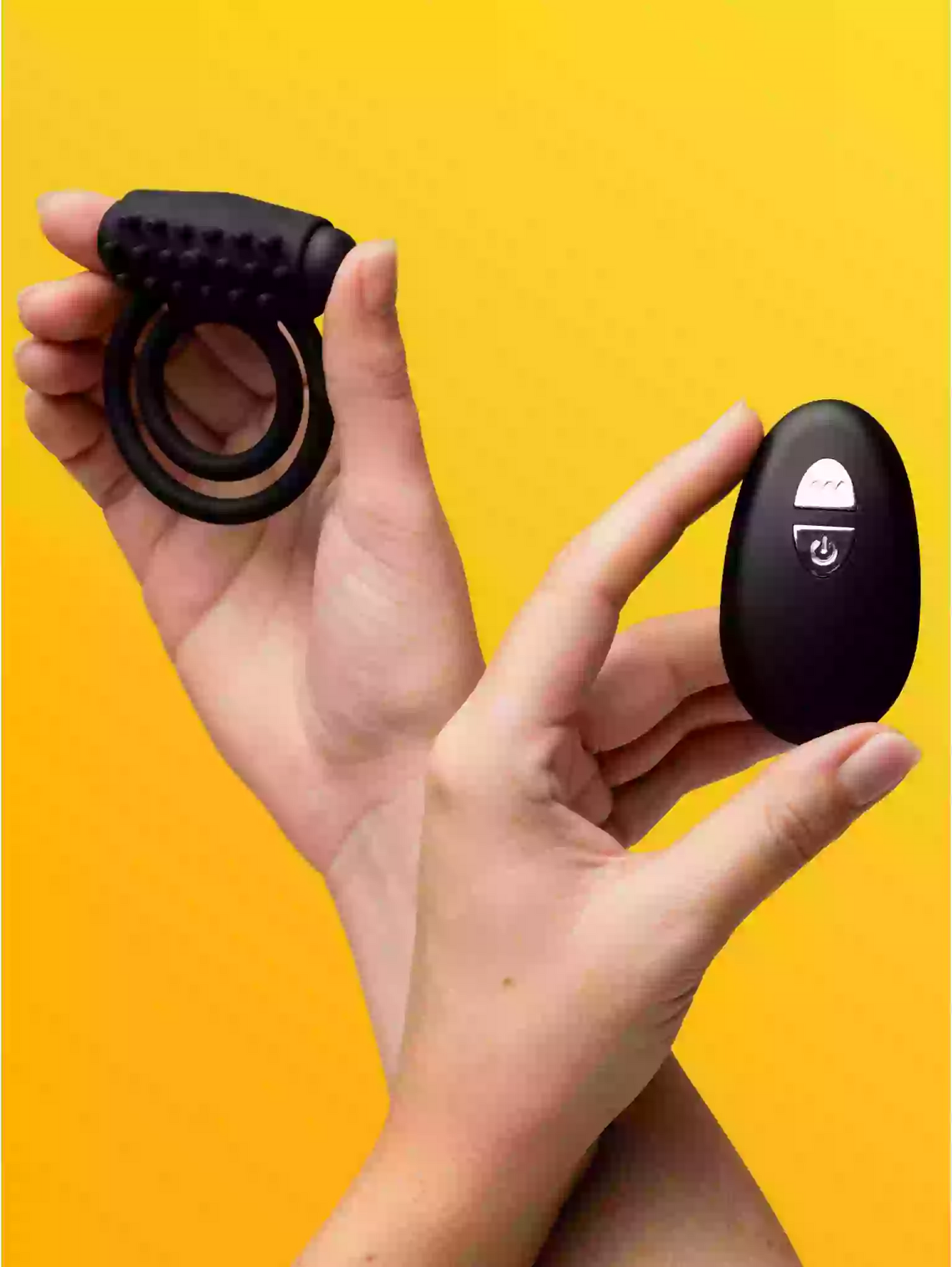 Black ring and remote control held by hands against a yellow background