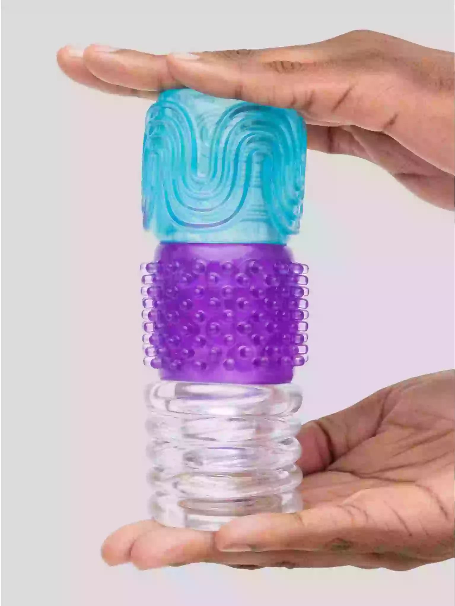 Hand holding a cylindrical massager with blue top and purple middle section on a light gray background