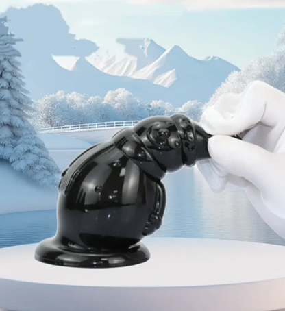 Black rubber duck being held by a gloved hand against a snowy mountain landscape