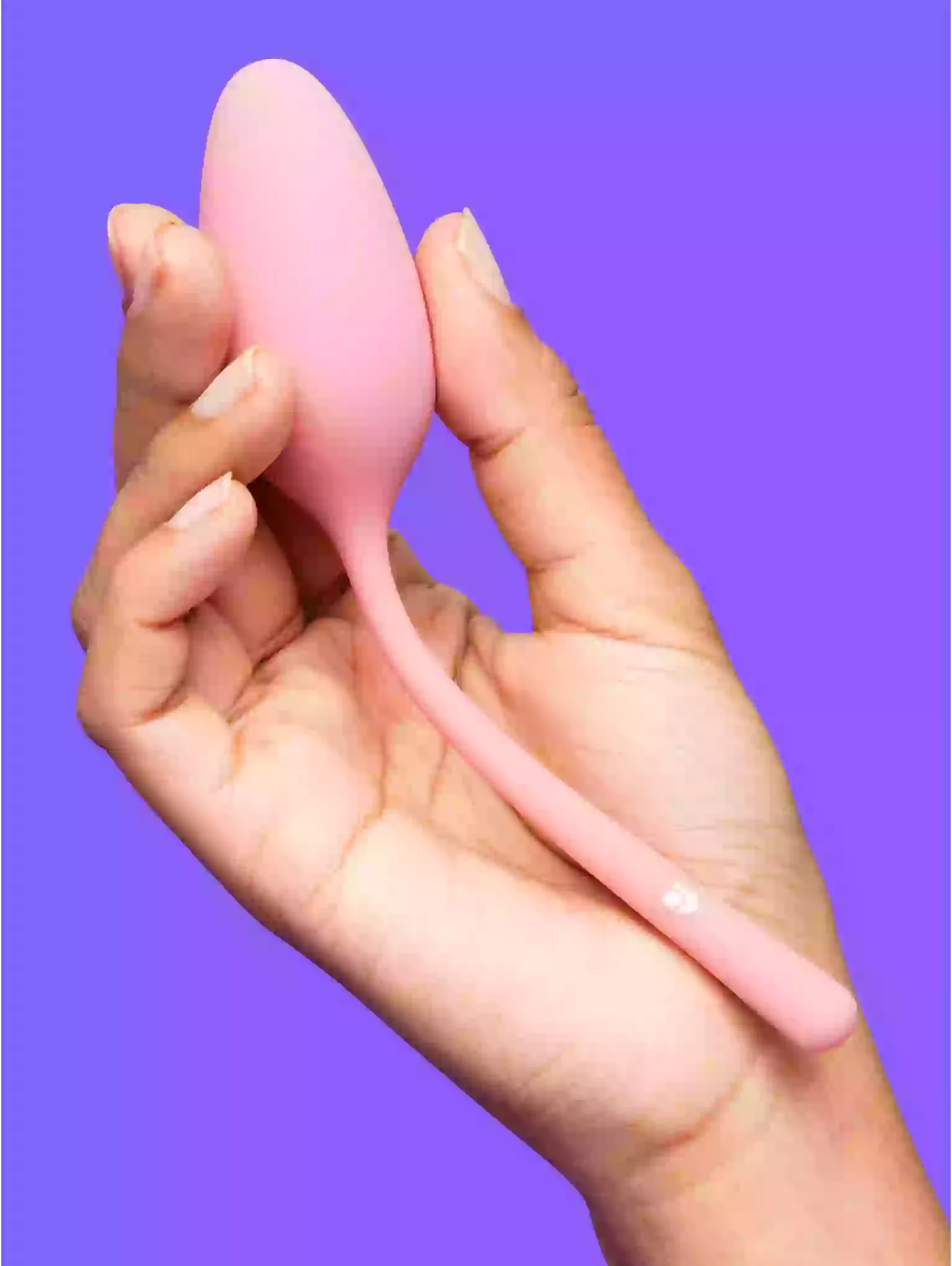Pink silicone tool held in a hand against a purple background